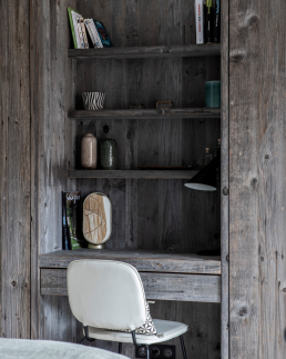 Petit chalet int&eacute;rieur coin bureau et rangement int&eacute;gr&eacute; en vieux bois gris&eacute; avec &eacute;tag&egrave;res, chaise blanche et lampe de table moderne.