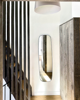 Petit chalet int&eacute;rieur entr&eacute;e moderne avec escalier &agrave; claire-voie en bois fonc&eacute;, miroir rectangulaire design sur mur blanc et armoire en vieux bois gris&eacute;.