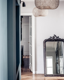 Couloir d&rsquo;appartement haussmannien avec parquet ancien, biblioth&egrave;que contemporaine sur mesure et miroir d&rsquo;&eacute;poque