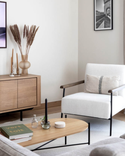 Coin salon avec fauteuil en tissu bouclette blanc aux accoudoirs bois, buffet en ch&ecirc;ne d&eacute;cor&eacute; de pampa s&eacute;ch&eacute;e et table basse ovale sur pieds noirs