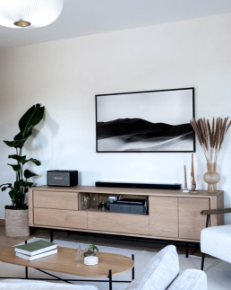 Meuble TV en ch&ecirc;ne sur pieds noirs, avec photographie noir et blanc de dunes et herbes de pampa dans un salon minimaliste
