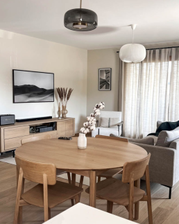 Salle &agrave; manger avec table ronde en ch&ecirc;ne, chaises assorties et suspension en verre fum&eacute;, ouverte sur salon avec canap&eacute;s gris