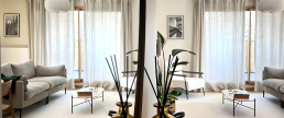 Salon lumineux avec canapés gris, tables basses ovales et grandes fenêtres habillées de rideaux en lin, vu en reflet de miroir