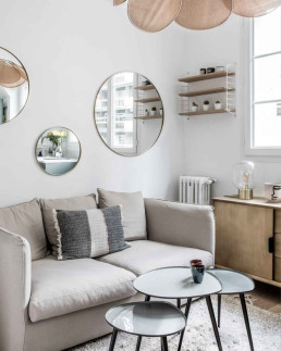 Salon petit appartement avec canapé beige et trio de miroirs ronds - Marque de Fabrik